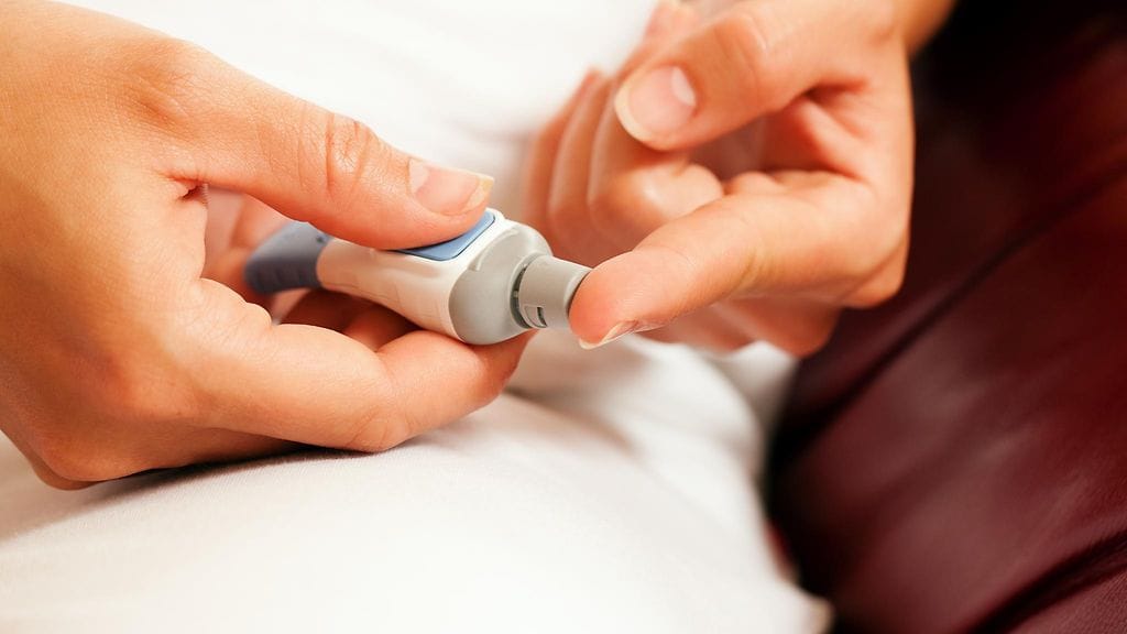 Kuvan nainen ottaa verinäytettä sormestaan verensokeritason mittausta varten.