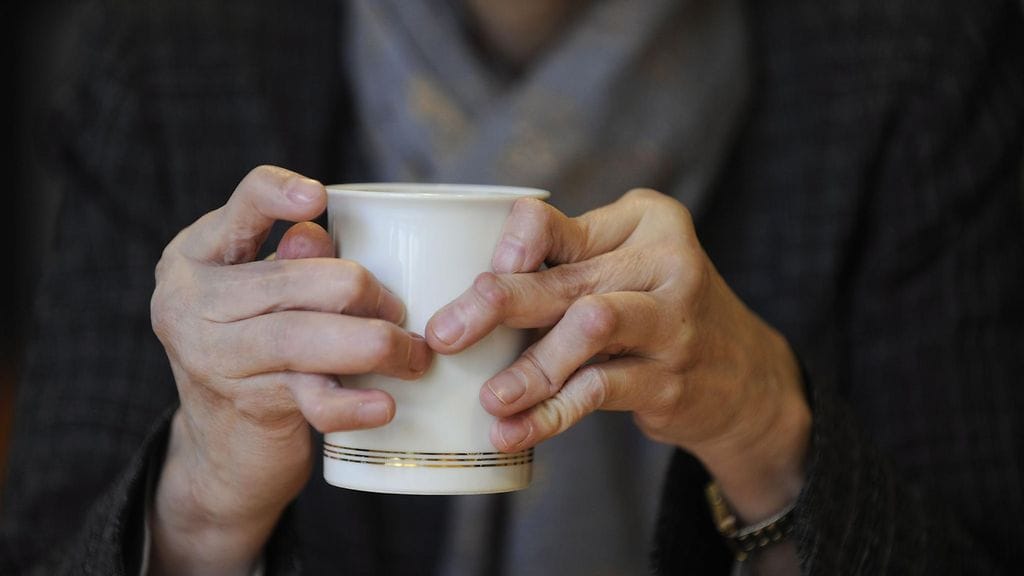 Reumasairas ihminen pitelee käsissään kahvikuppia.
