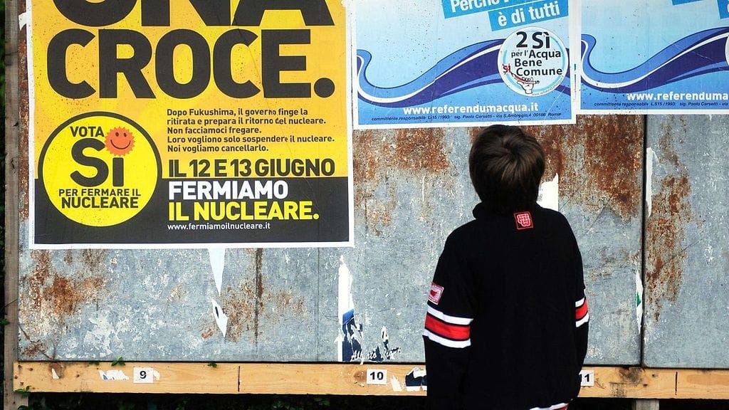 Poika katsomassa kansanäänestysjulisteita, joissa tuomitaan ydinvoiman ja veden yksityistäminen Corbettassa, Länsi-Milanossa. Kuva on vuodelta 2011.