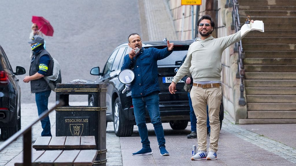 Salwan Momika ja hänen ystävänsä Ruotsin parlamentin edessä maanantaina. Salwan polttaa koraania.