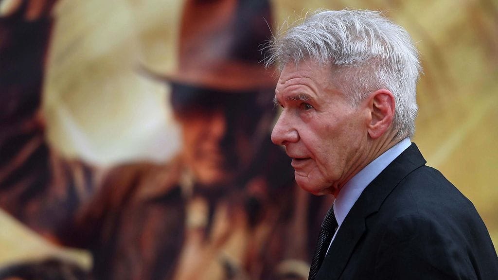 Näyttelijä Harrison Ford. Taustalla näkyy kuva ikonisesta Indiana Jones -hatusta.