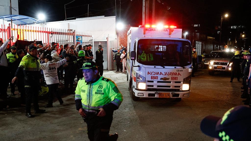 Ambulanssi ajaa vilkut päällä öisellä kadulla ihmisten parveillessa ympärillä.